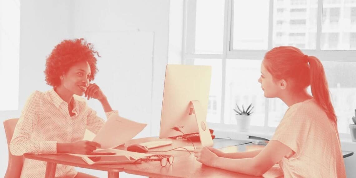 two women sitting at a desk with a computer